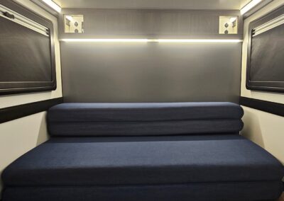 Interior view of the CORE RV 5510 rear interior with foldable sofa (queen bed) and upper storage with side cubbies and a passthrough to the back galley