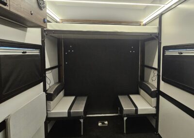 Interior rear view of the CORE 6515 Trailhead with dinette seats in the seated position and the upper bunk in place