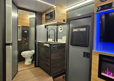 Interior view of CORE RV with fireplace illuminated, and backlit TV lighting. Looking towards the front of the trailer and looking at the kitchen and bath.