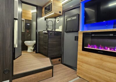 Interior view of CORE RV with fireplace illuminated, and backlit TV lighting. Looking towards the front of the trailer and looking at the kitchen and bath.