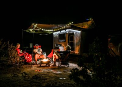 CORE RV 5510 unit shown at night near a campfire with people sitting around, lights hanging from the awning