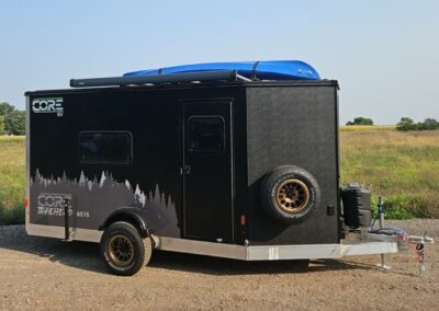 Exterior view of the CORE RV 6515 Trailhead curbside with grey tree graphics and awning on the roof and a mounted kayak